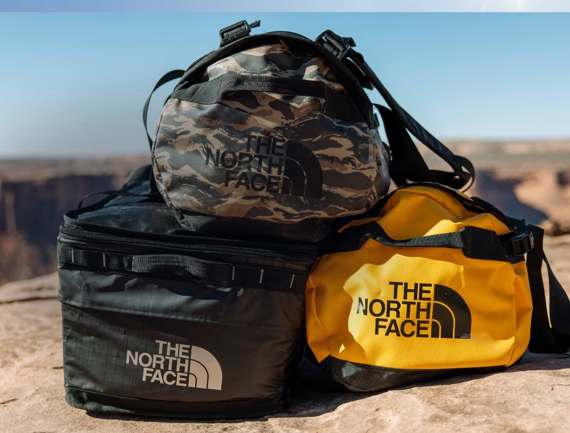Three North Face Base Camp duffel bags in black, green, and yellow, showcasing its durable design and spacious interior for travel and outdoor use.