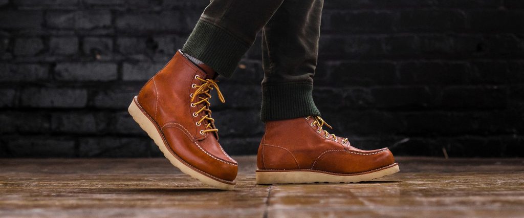 Close-up of a man's feet in a red wing moc toe boot, showcasing the rich leather texture and unique stitching details.