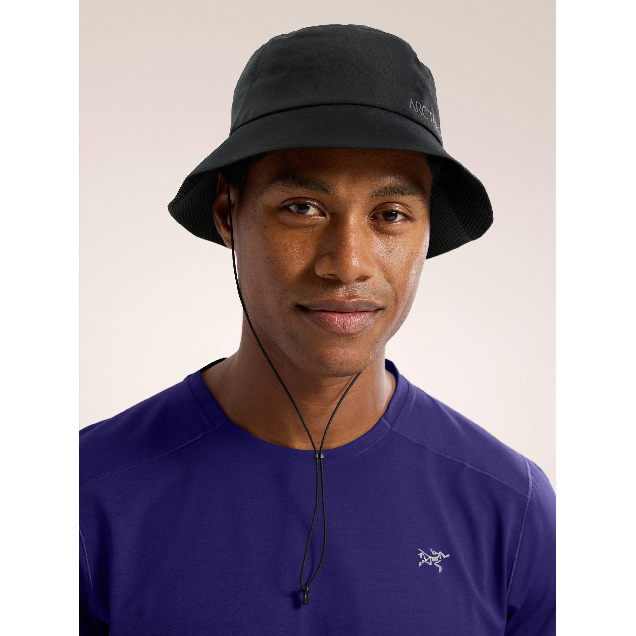 Person wearing a black Arc'teryx bucket hat with a chin strap and a purple technical t-shirt.