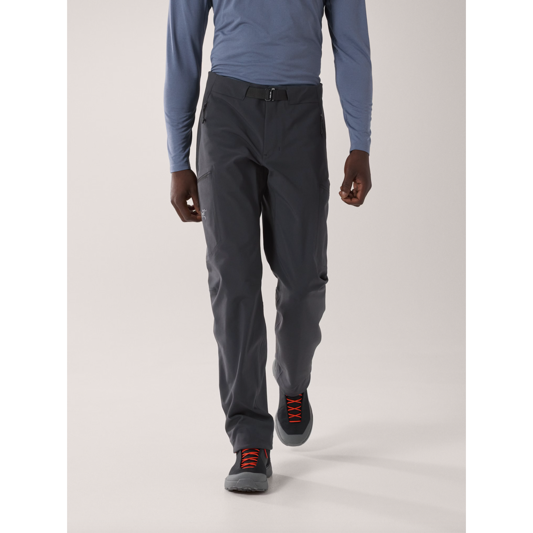 Model wearing charcoal grey Arc'teryx technical hiking pants with an integrated belt and zippered pockets.
