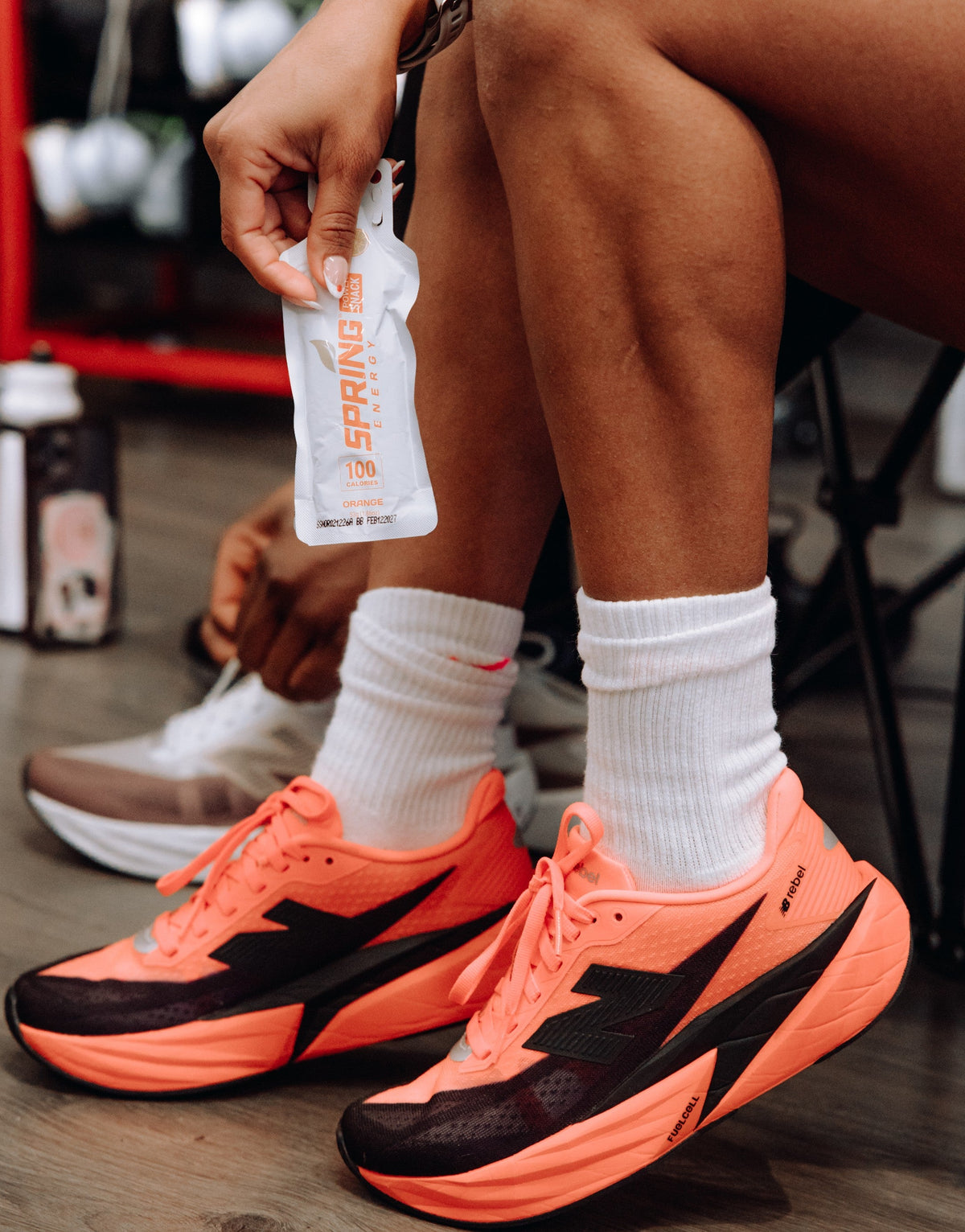 Person holding a Spring Energy gel packet while wearing bright orange running shoes and white crew socks.