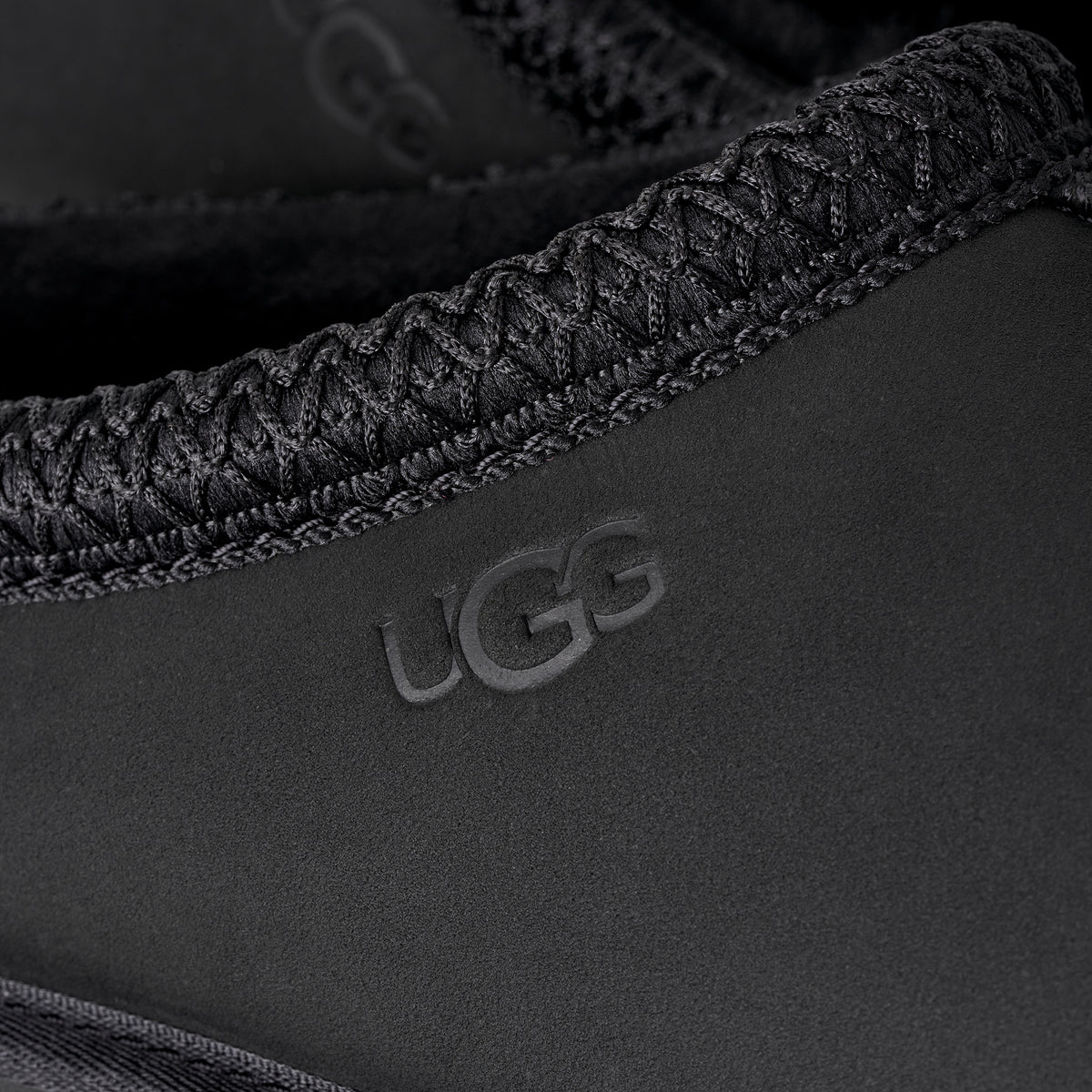 Close-up of black UGG Tasman II nubuck slipper featuring signature UGGbraid collar detail and heat-embossed logo.