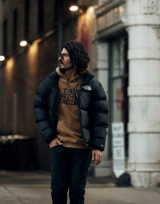 A man walks outdoors wearing a North Face jacket over a North Face shirt,
showcasing the jacket's stylish design.