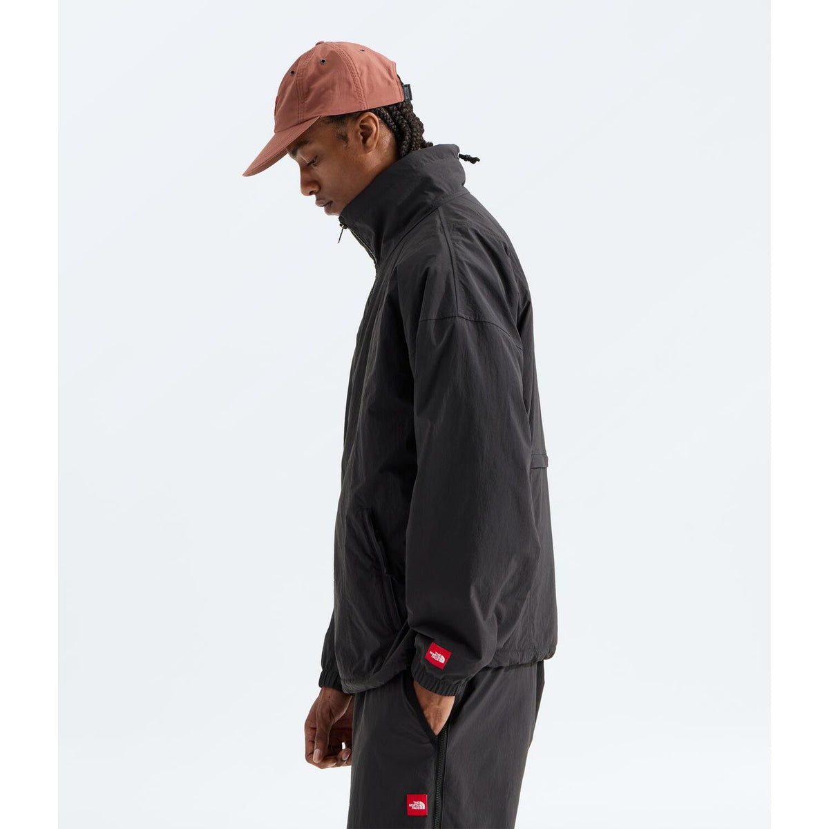 Man wearing a black oversized North Face WindWall nylon jacket with a red box logo patch on the sleeve.